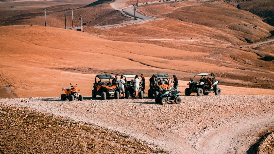 Off-road vehicles and people on a dusty desert hill.